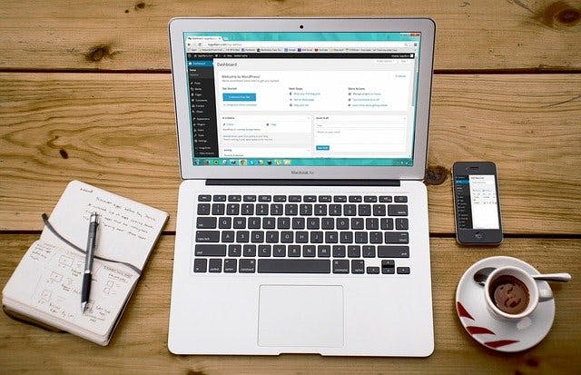 Laptop neben Kaffeetasse, Smartphone und Notizblock