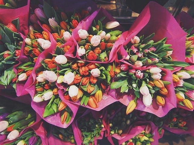 Gestapelte, bunte Tulpensträuße in rosa Papier