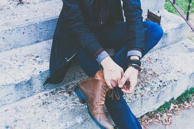Mann mit Jeans, Mantel, Hemd und Lederschuhen sitzt auf Betontreppe