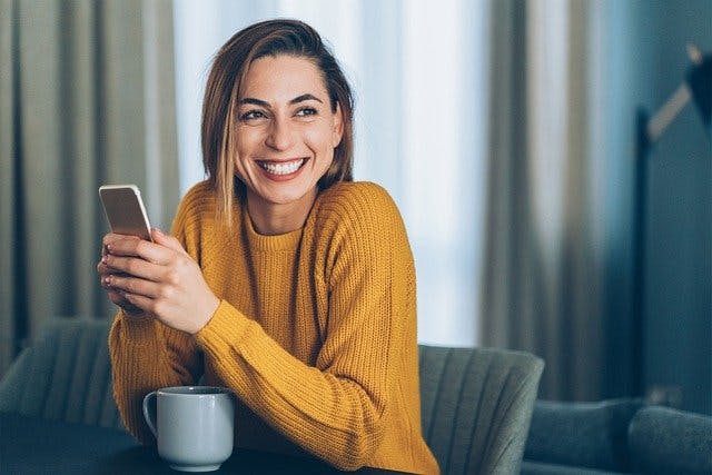 Fröhliche Frau mit Handy und Kaffee