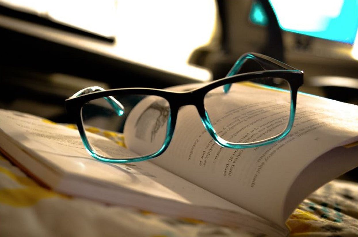 Gutscheine.de Kategorie Brillen Kontaktlinsen Türkisschwarze Brille auf aufgeklapptem Buch