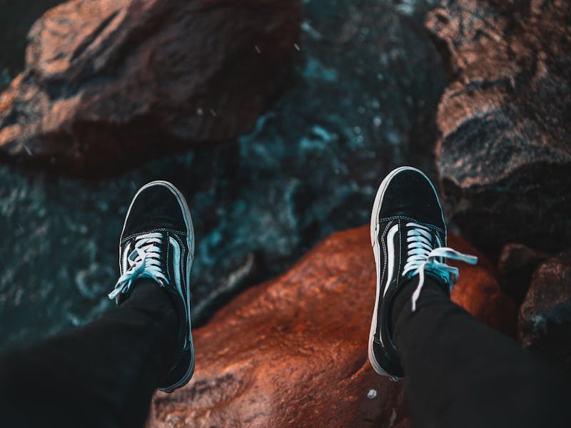 Person lässt Füße mit Vans Schuhen über Steilküste baumeln