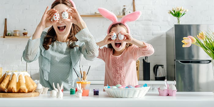 Ostern 2021: Gutscheine und Angebote für tolle Geschenke Mutter und Tochter stehen gemeinsam in der Küche und halten sich Ostereier vor die Augen