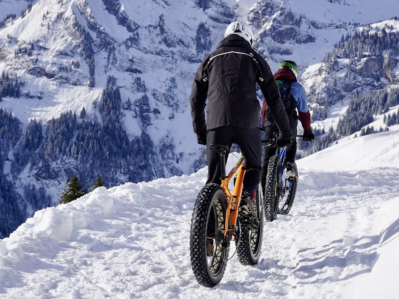 Zwei Fahrradfahrer fahren einen verschneiten Weg auf einem Bergweg entlang.