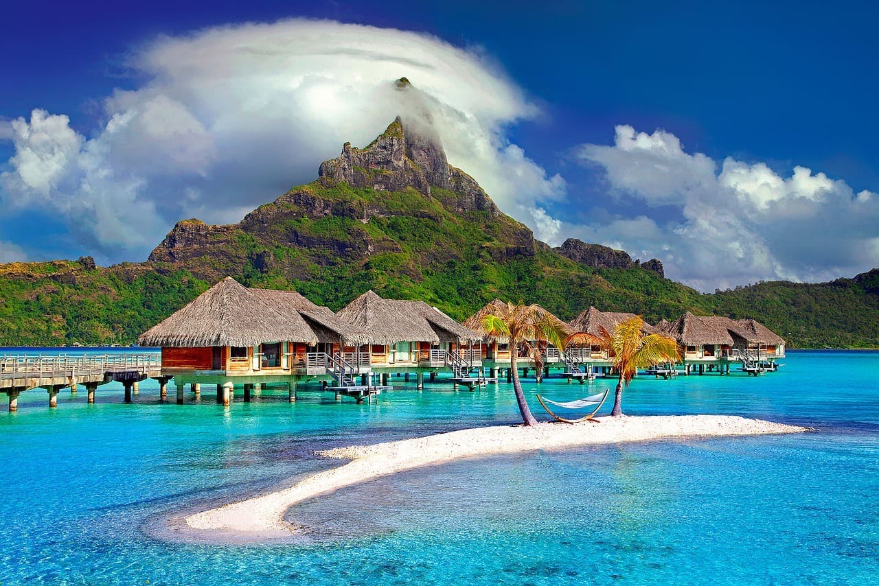 Berge_und_Meer_Insel Kleine Hütten im Meer, spitzer Berg dahinter