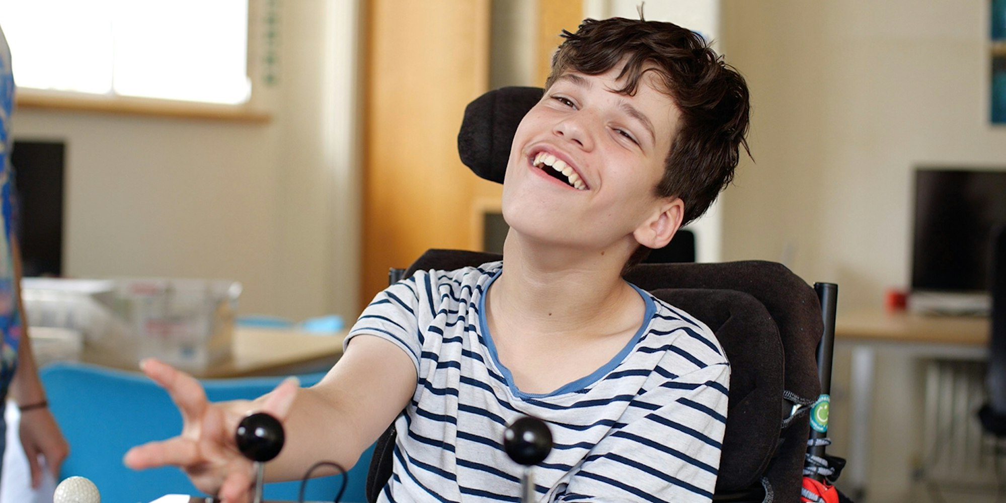 a young boy wearing a blue and white striped tshirt plays with two large joysticks