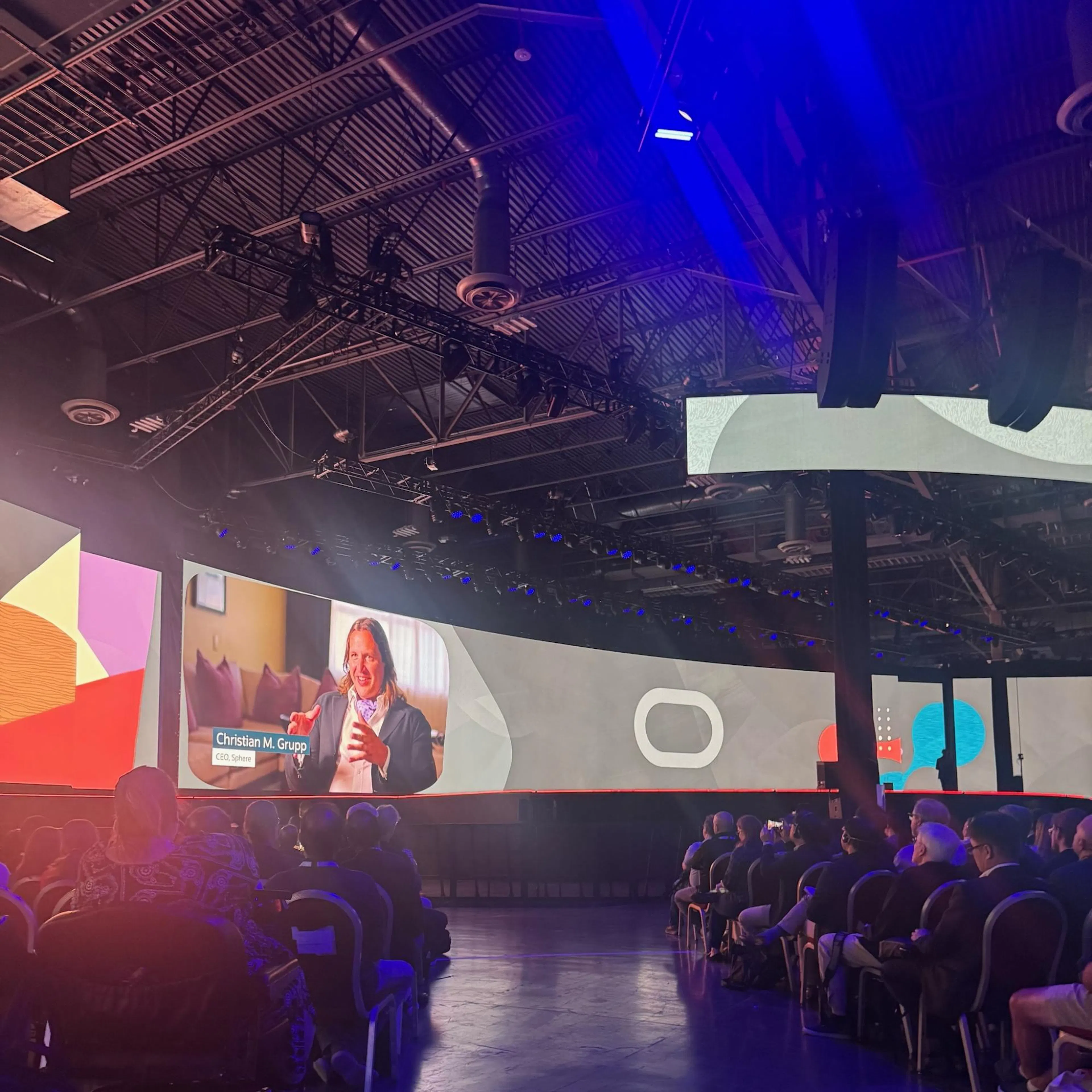 Audience at an Oracle AI World 2025 keynote watching Sphere CEO Christian M. Grupp on a large curved screen.