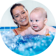A lady smiling holding a smiling baby in a pool