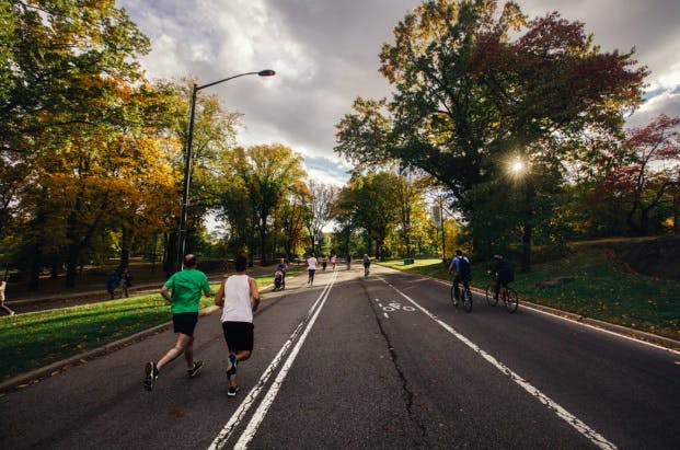 Two men running on a road near a park.