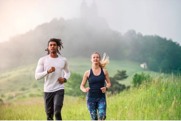 Man and woman running together, with a misty forest behind them
