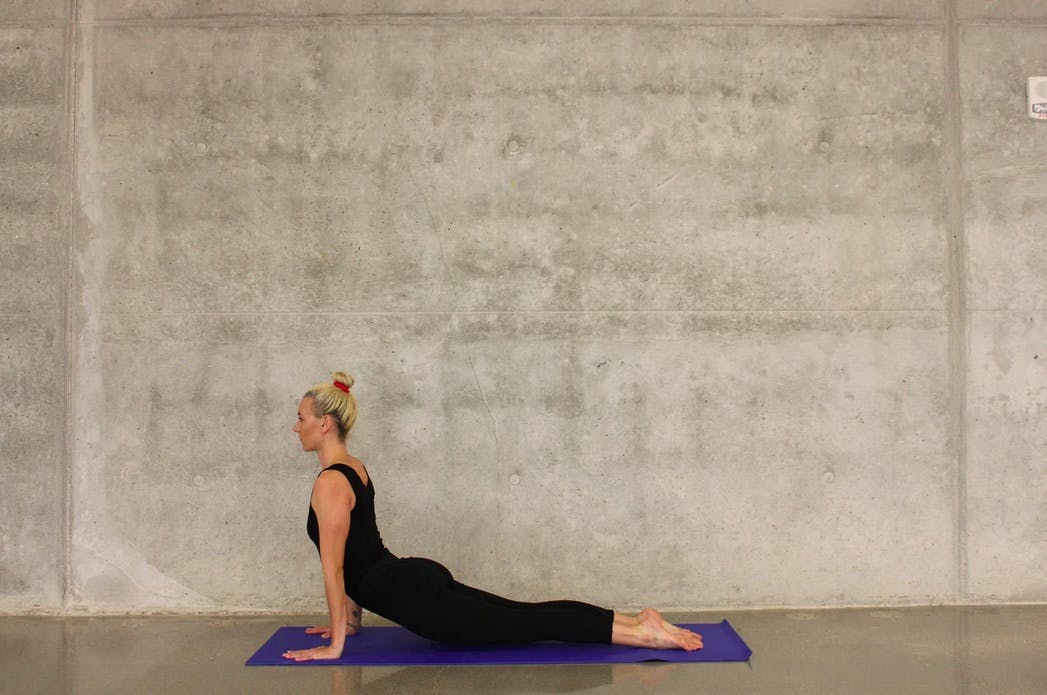 Blonde woman doing yoga on the floor, in front of a concrete wall