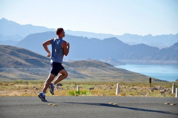 Man running on a road near hills.