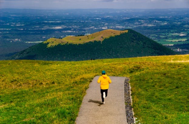 Man with yellow jacket running in a hilly landscape
