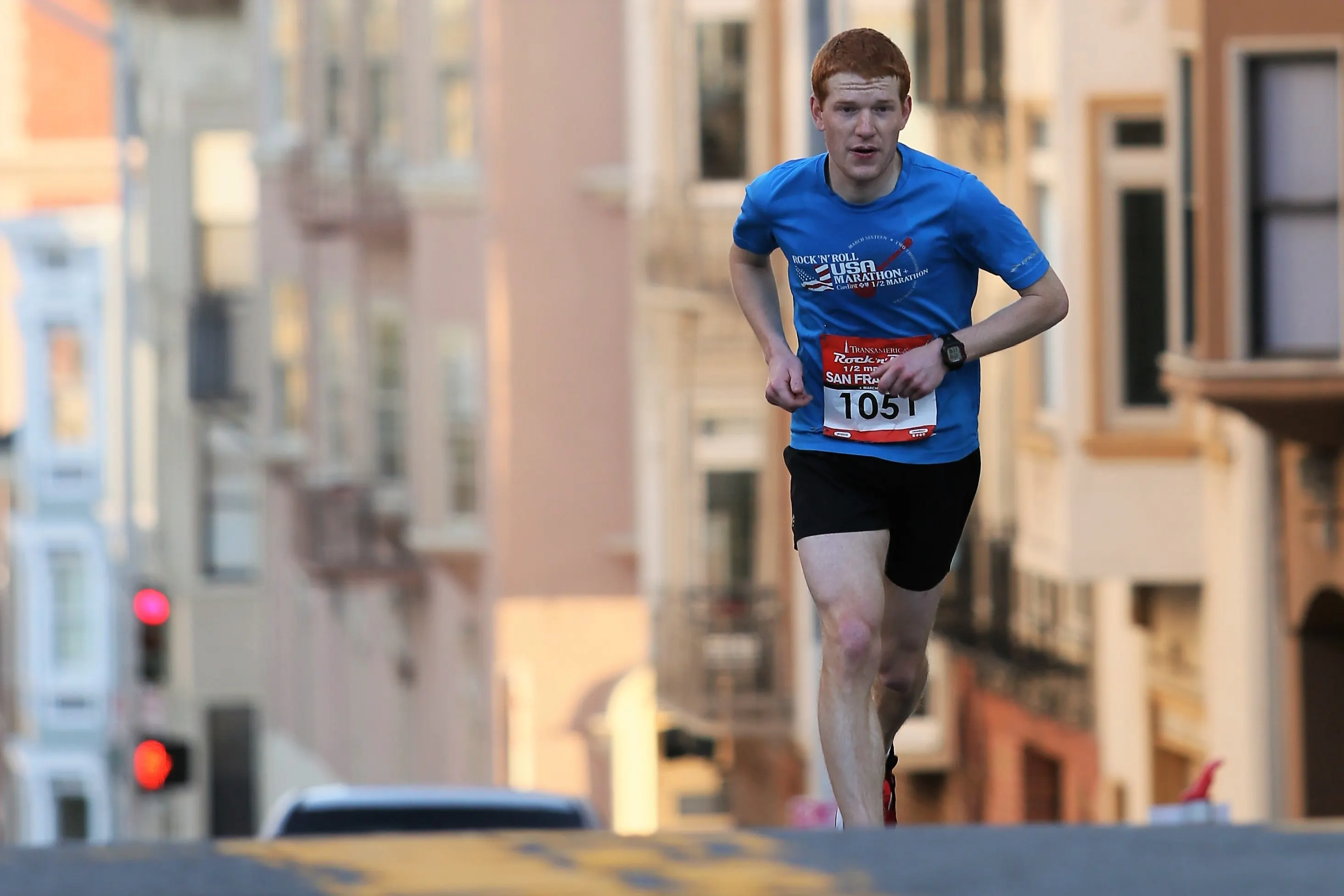 Young man wearing a blue T shirt, running a marathon in the city