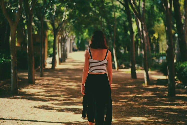 Image of a dark haired woman walking in the park in the summer