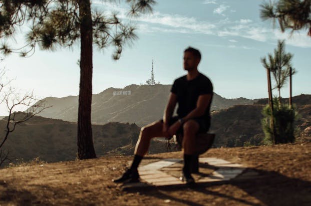 Man sitting on the top of the hill. Hollywood sign can be seen behind. 