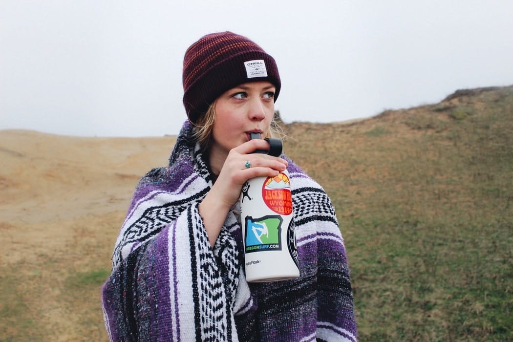 Blonde woman dressed in a colorful poncho, drinking water