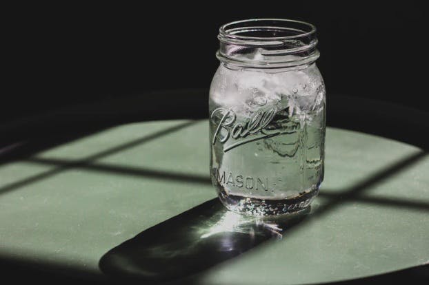 A jar full of water on a table and its reflection