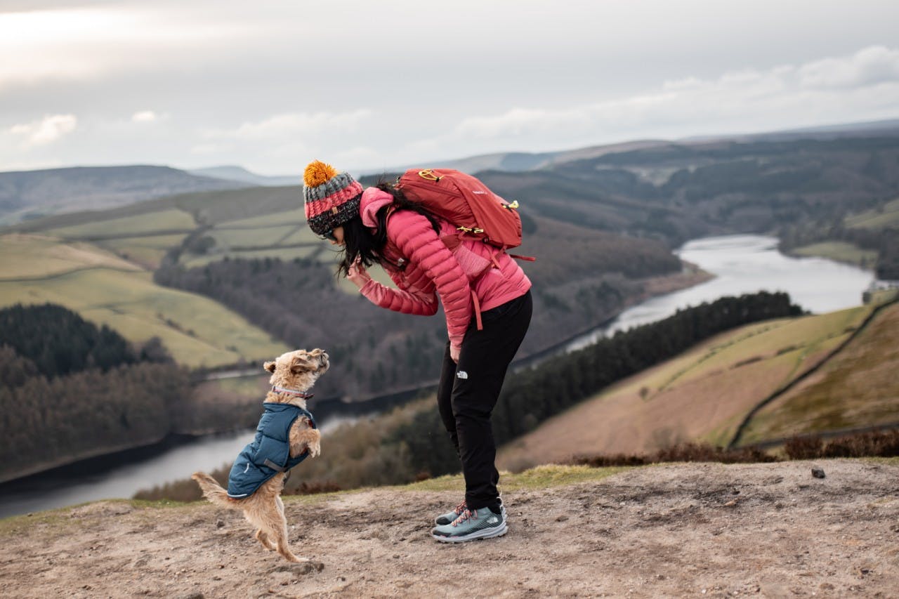 Maria und ihr Hund (auf den Hinterbeinen) auf einem Felsvorsprung mit Peak District im Hintergrund