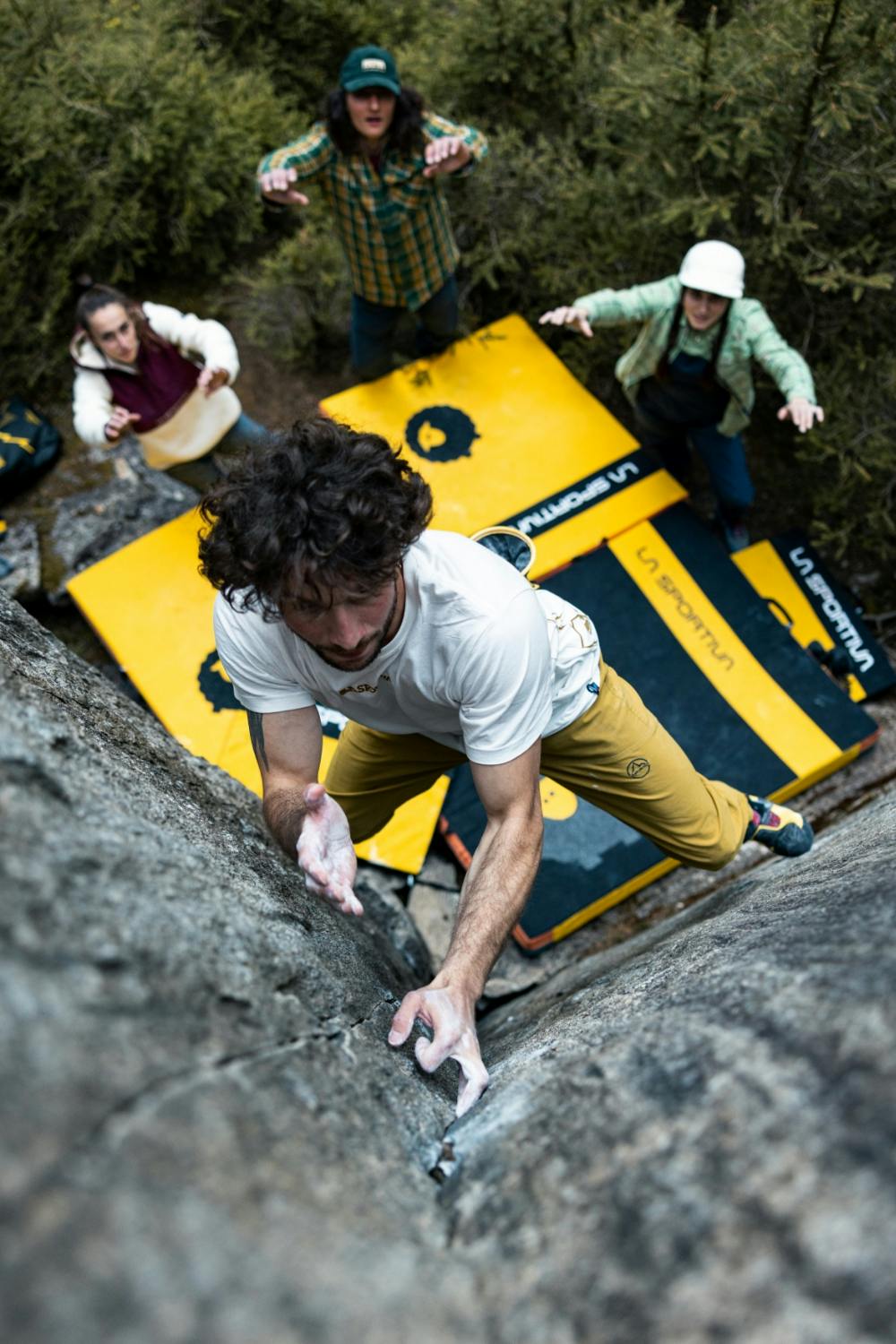 A rock climber in a white shirt scaling a steep granite face using La Sportiva climbing shoes and technical mountain gear.