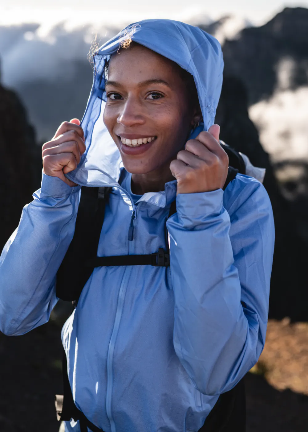 woman in blue jacket with hood up on the mountains
