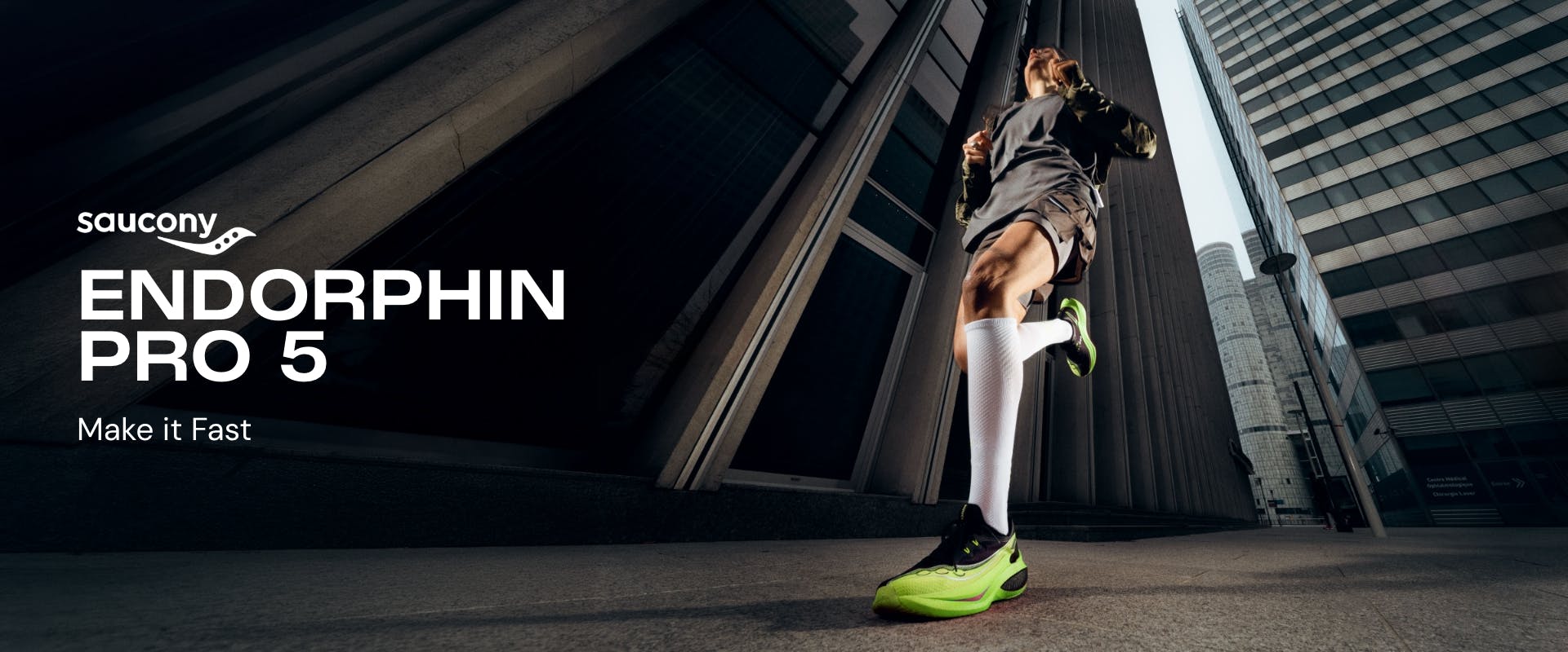 Saucony Endorphin PRO 5 running shoes in lime green and black. A runner in motion against a backdrop of modern city skyscrapers. Text: Saucony Endorphin PRO 5 - Make