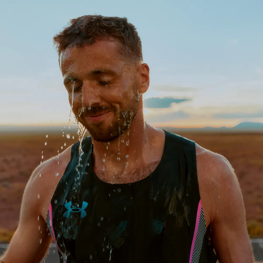 Portrait of a perspiring male runner in a black Under Armour tank top against a desert sunset background for the men's training gear line.