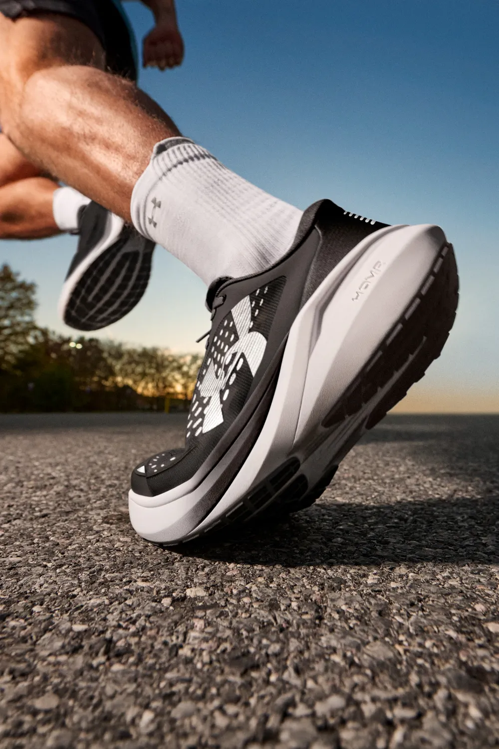 Action close-up of a runner's foot in a black and white Under Armour Velociti running shoe hitting the pavement.
