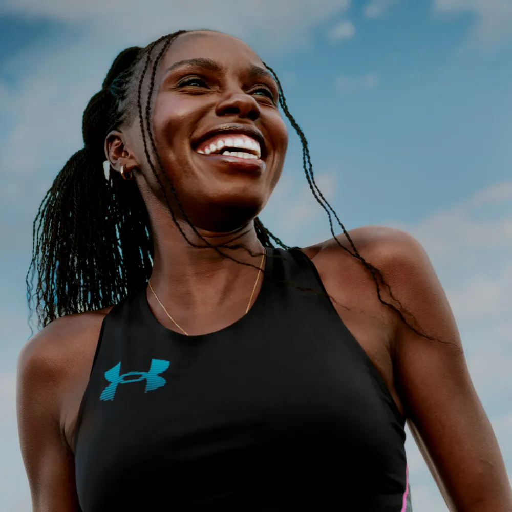 Smiling female athlete wearing a black Under Armour performance tank top with the teal UA logo for the women's athletic apparel collection.