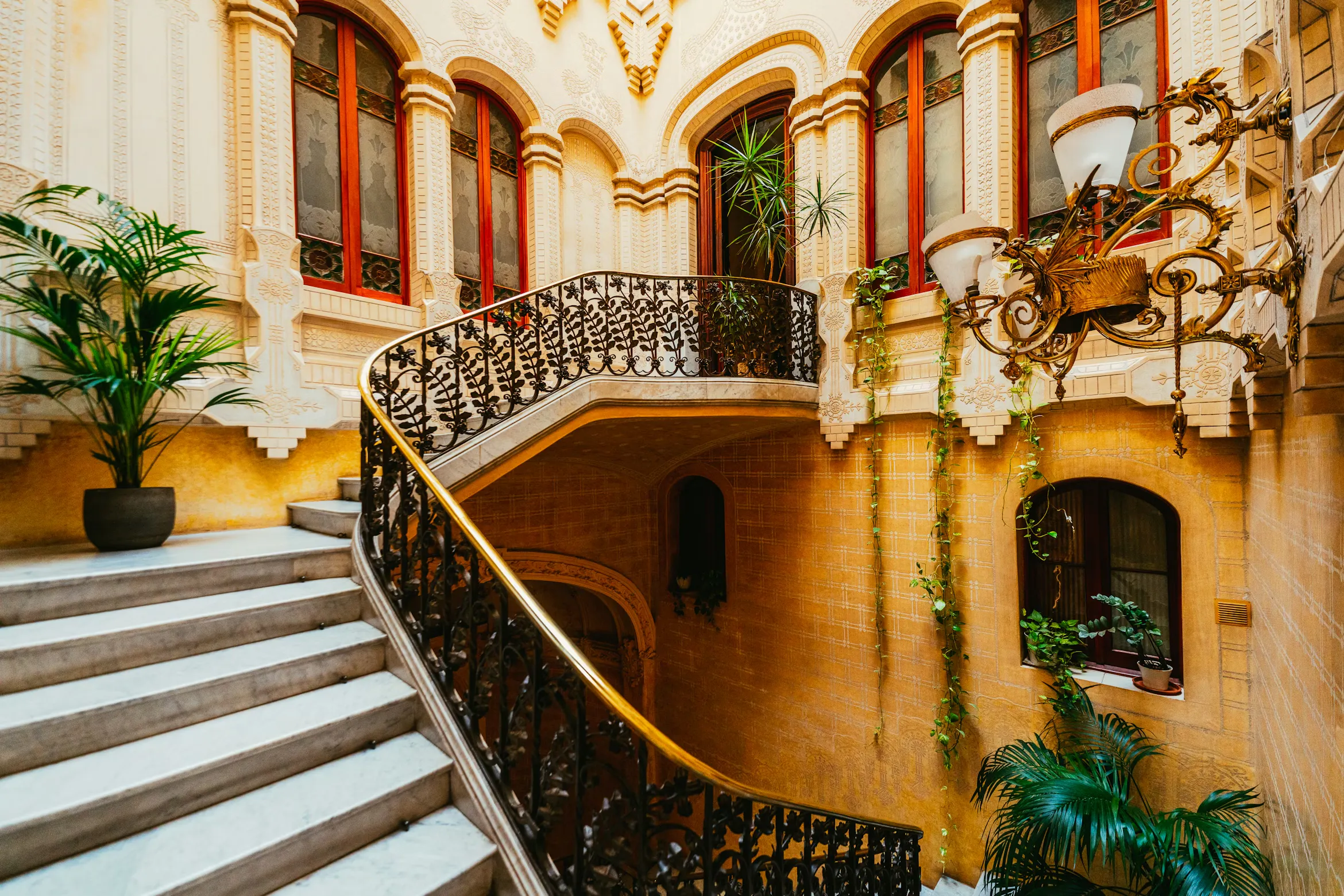 Elegant escala de marbre en un edifici modernista de luxe a Barcelona, amb baranes de ferro forjat ornamentades, arquitectura d'època i llum natural.