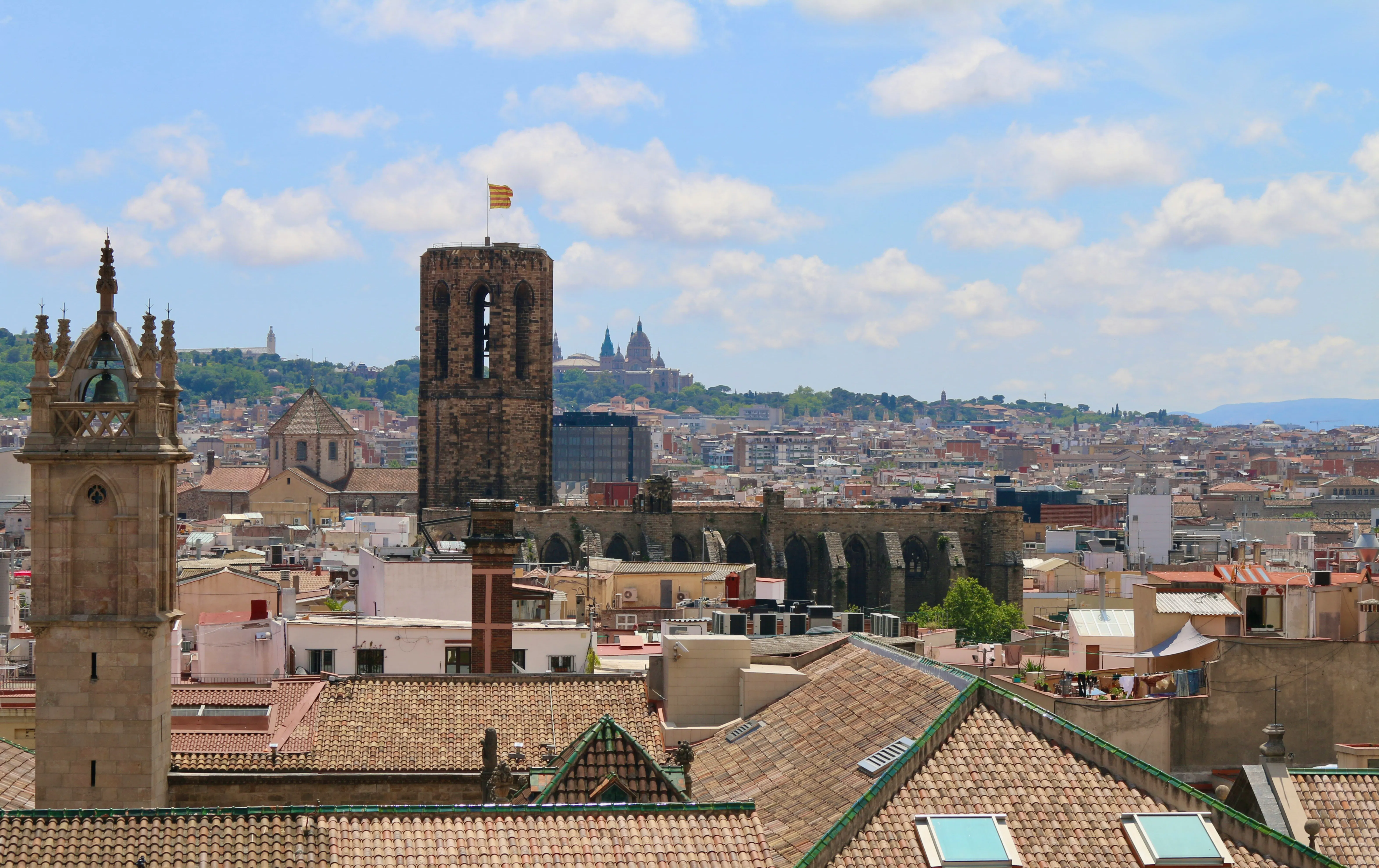 Vista panorámica del Barrio Gótico de Barcelona con tejados históricos, torres de iglesias y Montjuïc al fondo.