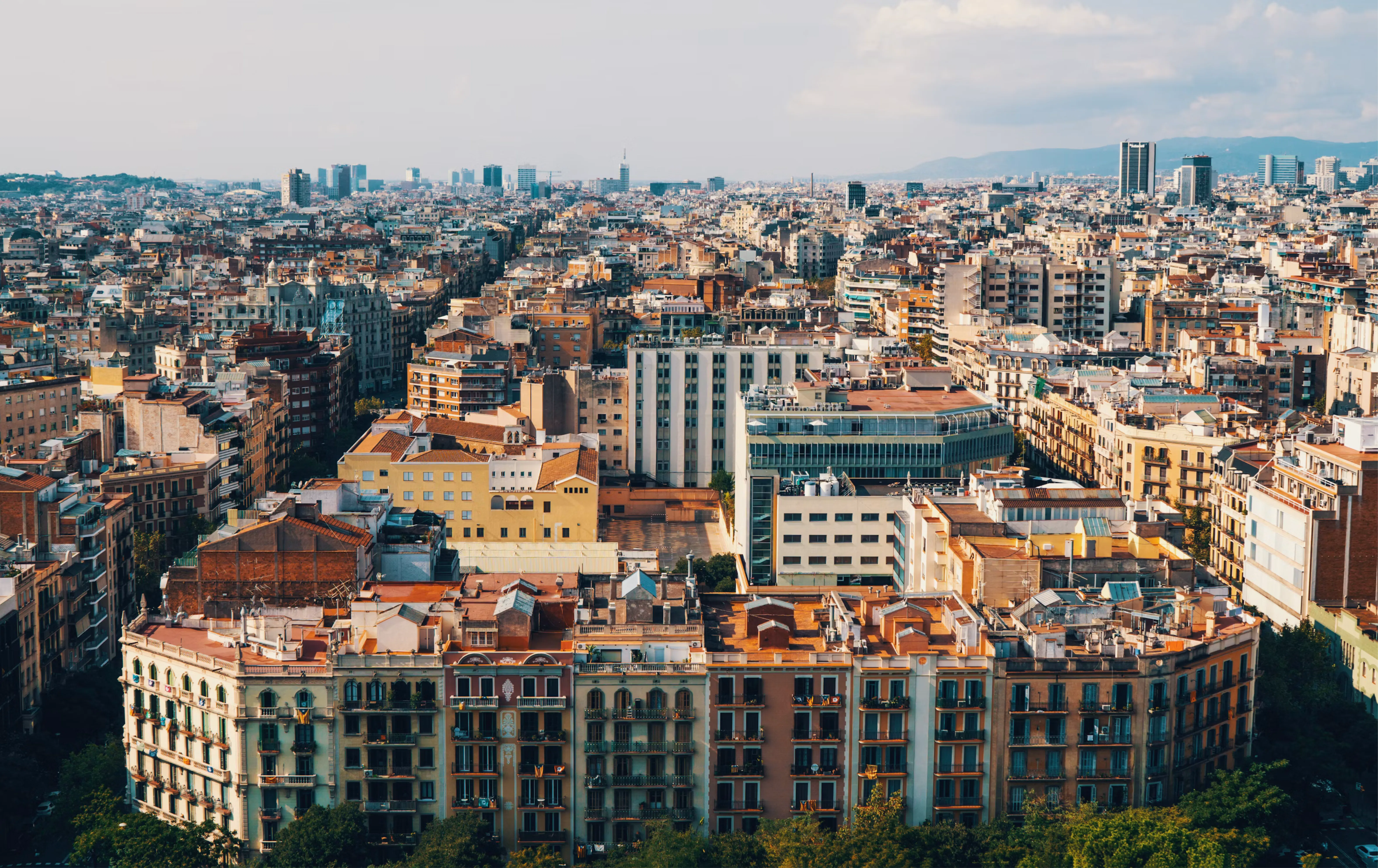 Vista aèria del districte de l’Eixample de Barcelona amb edificis residencials, terrats i l’skyline de la ciutat, mostrant l’estil de vida urbà del centre de Barcelona.