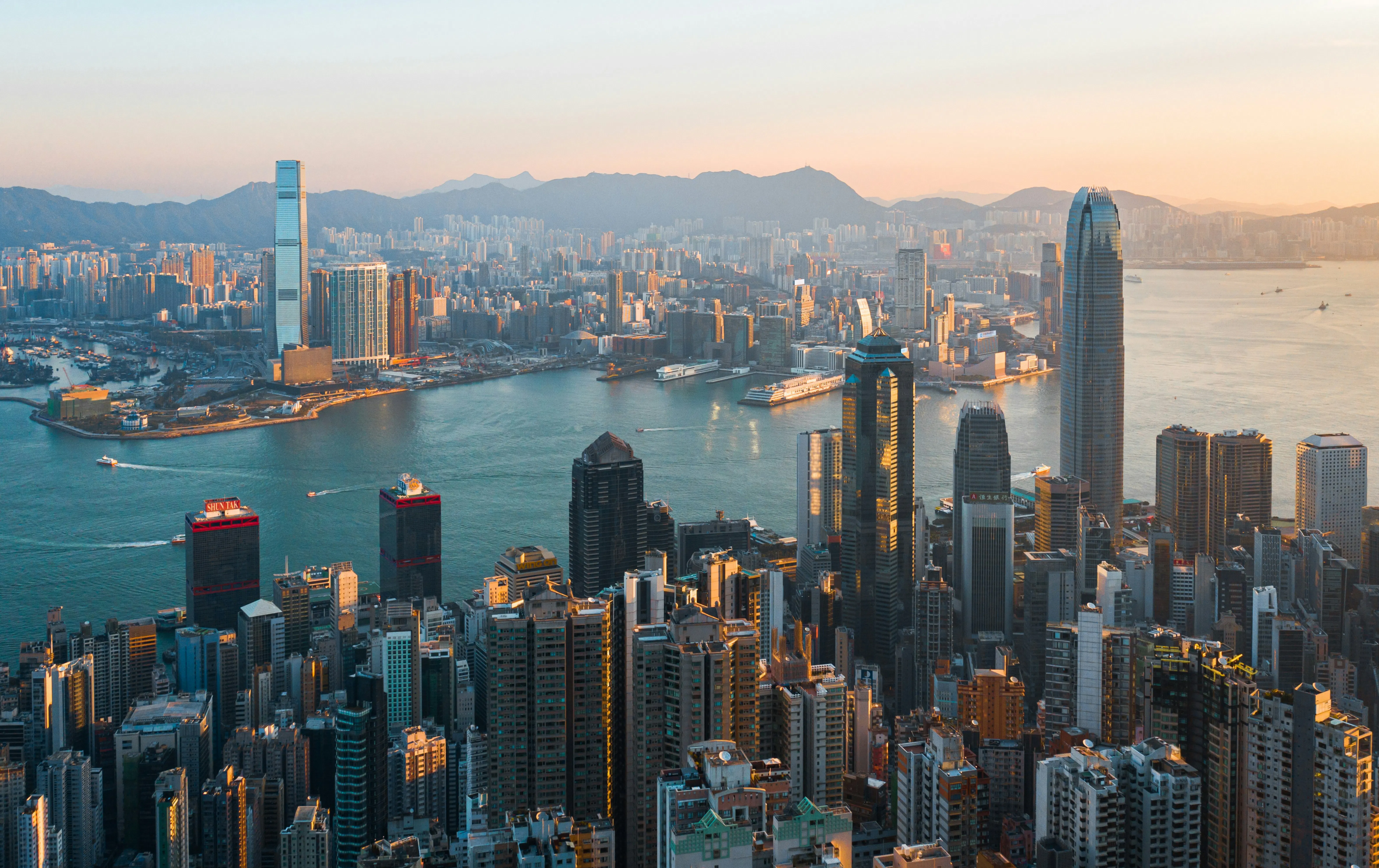 Vista aèria de l’skyline de Hong Kong i Victoria Harbour al capvespre, amb gratacels, zones davant del mar i el mercat immobiliari urbà.