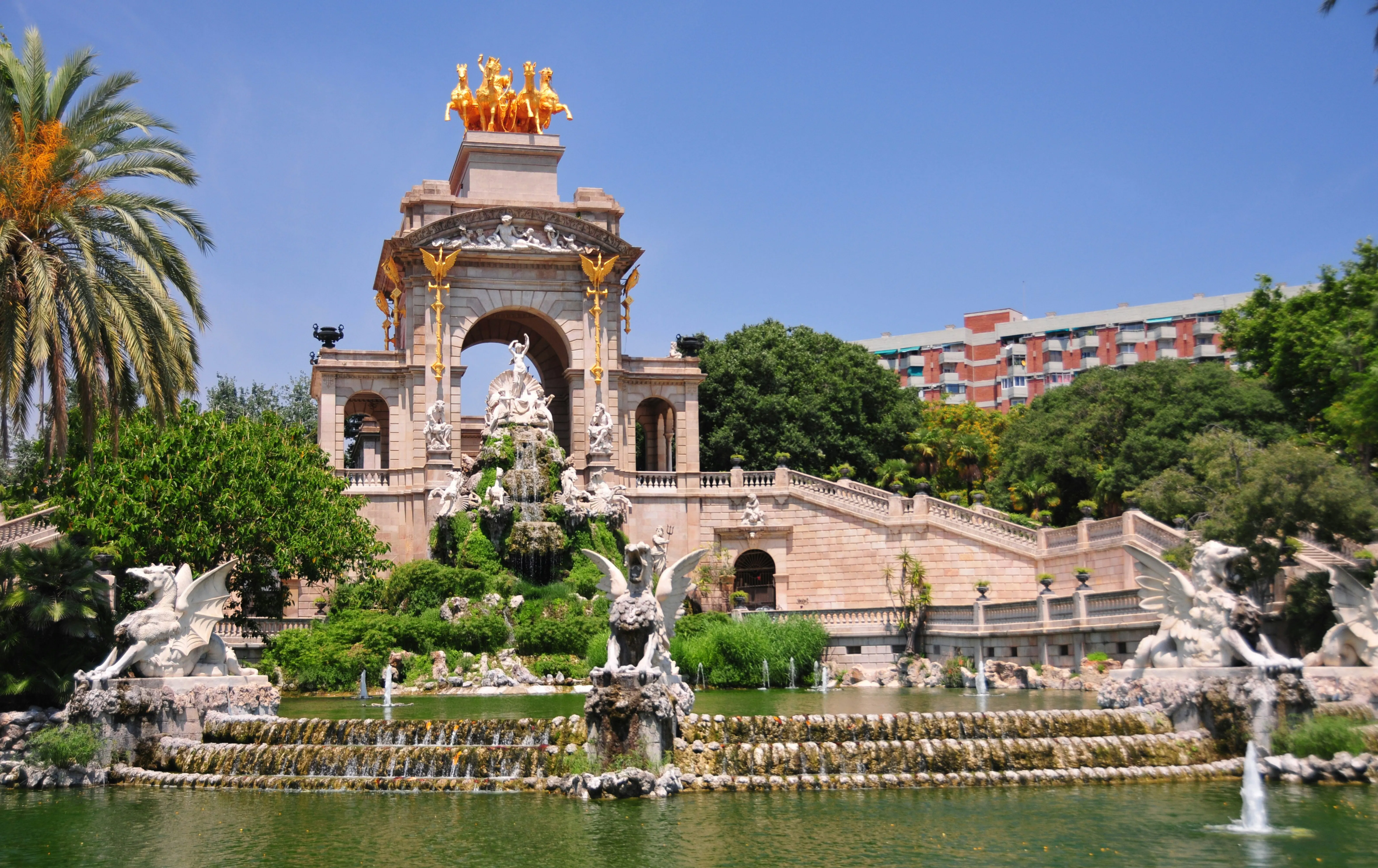 Monumentaler Wasserfall und Brunnen im Parc de la Ciutadella in Barcelona, umgeben von Palmen und Grünanlagen.