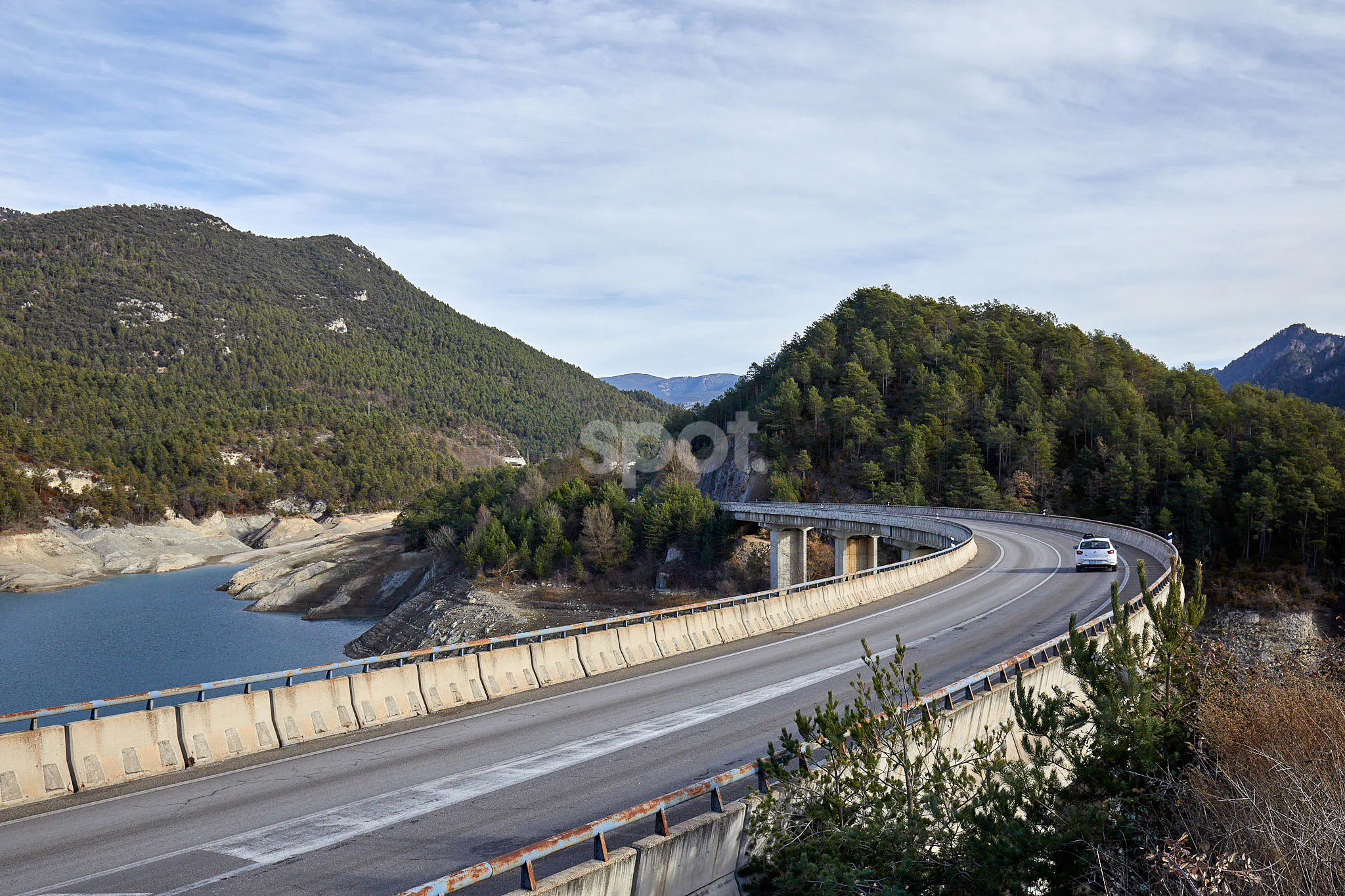 Bergstraße mit Brücke als Filmlocation in Spanien mit bewaldeten Hügeln, Blick auf einen Stausee, weiten Kurven und Auto für Automotive-Produktionen.