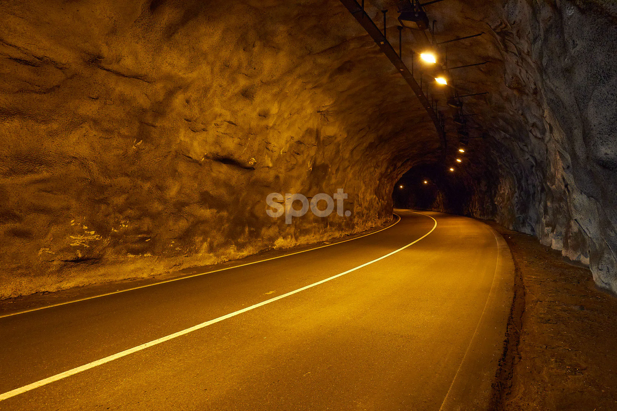 Localización de rodaje en un túnel de carretera en España con luz cálida, carretera curva y paredes rocosas para anuncios de coches y escenas de conducción cinematográficas.