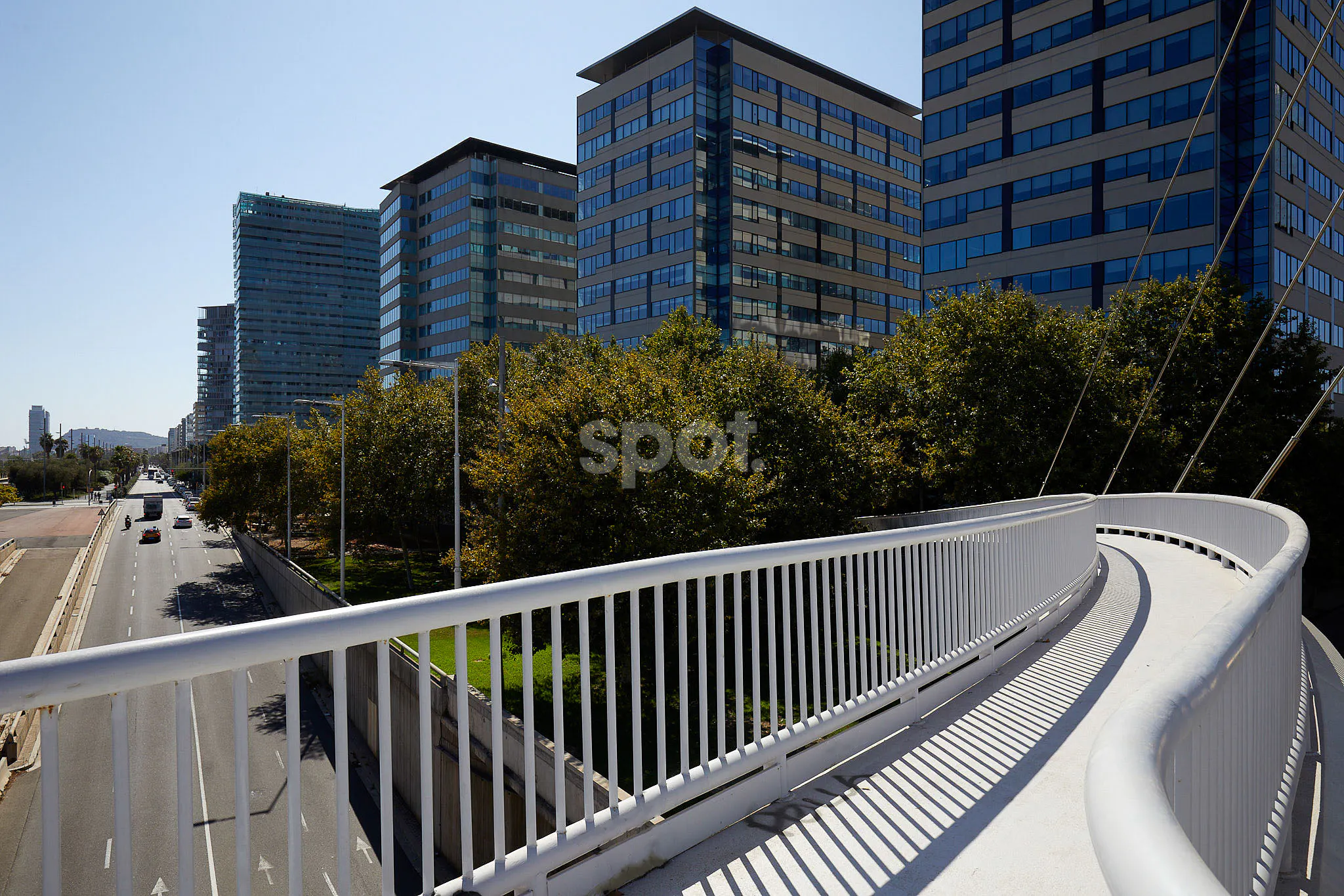 Urban filming location with modern office towers, elevated white bridge, wide road, trees and business district architecture.