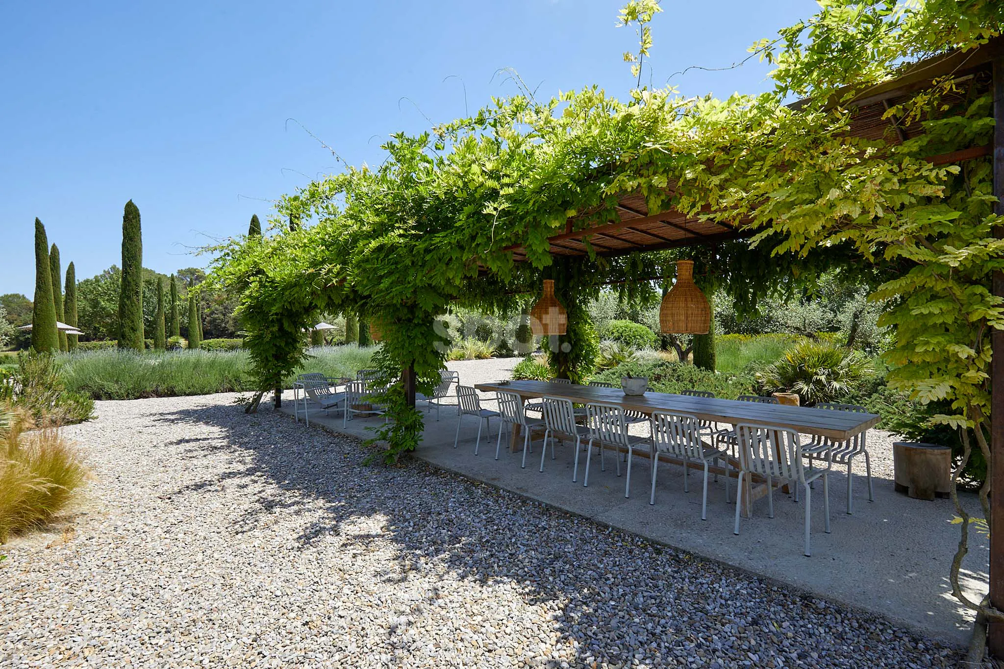 Localización de rodaje en terraza ajardinada de una villa de lujo en España con pérgola cubierta de vegetación, comedor exterior, caminos de grava, cipreses y paisajismo mediterráneo.
