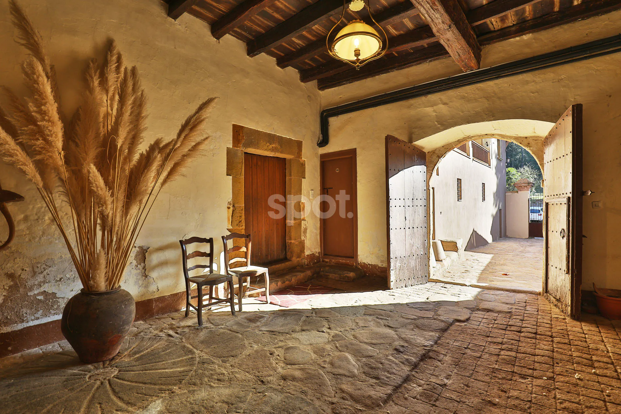 A rustic entrance hall of a traditional Spanish country estate featuring stone flooring, exposed wooden beams, old wooden doors, and warm earth tones for film backdrops.