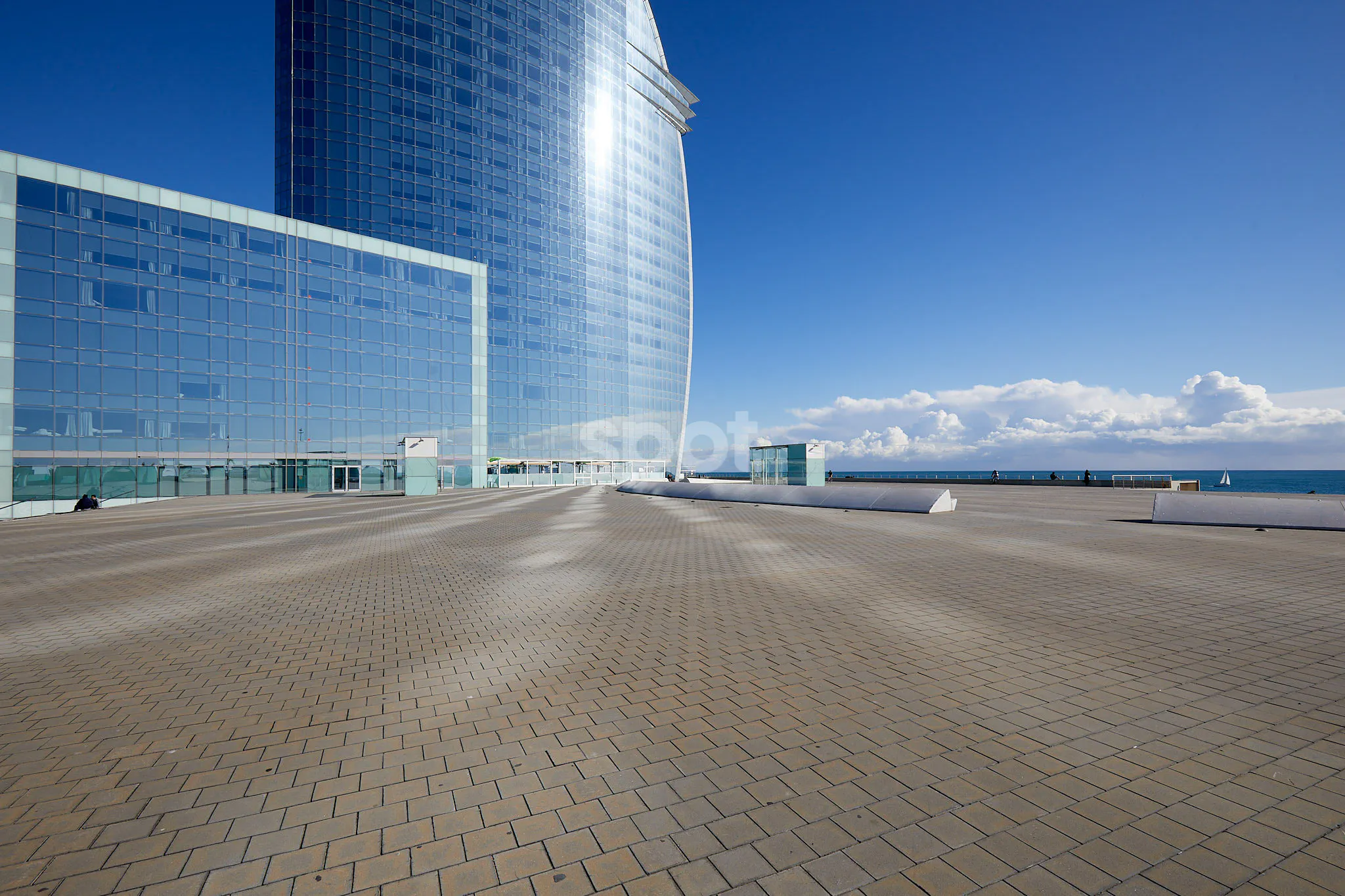 Barcelona seafront filming location with modern glass architecture, open paved plaza, sea views and clear blue sky.