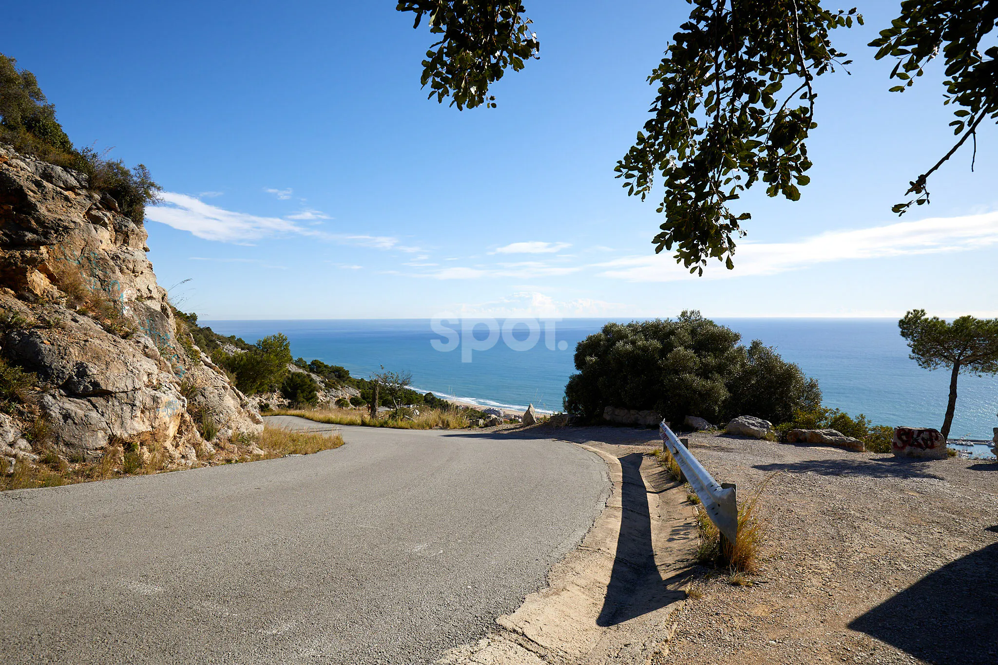 Coastal road filming location in Spain with sea views, rocky cliffs, Mediterranean trees, blue sky and natural sunlight.