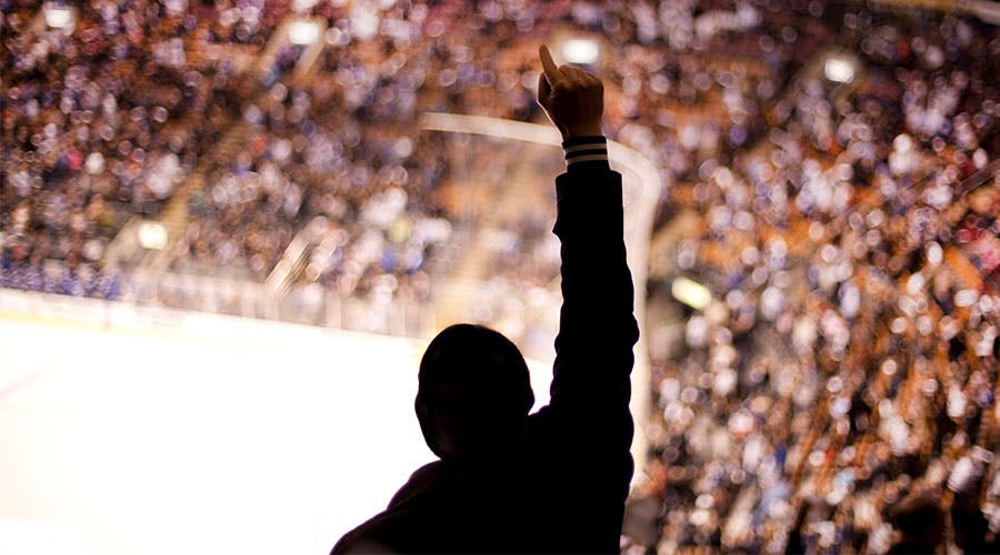 The silhouette of a person with their arm raised in triumph while in the crowd at a sports arena