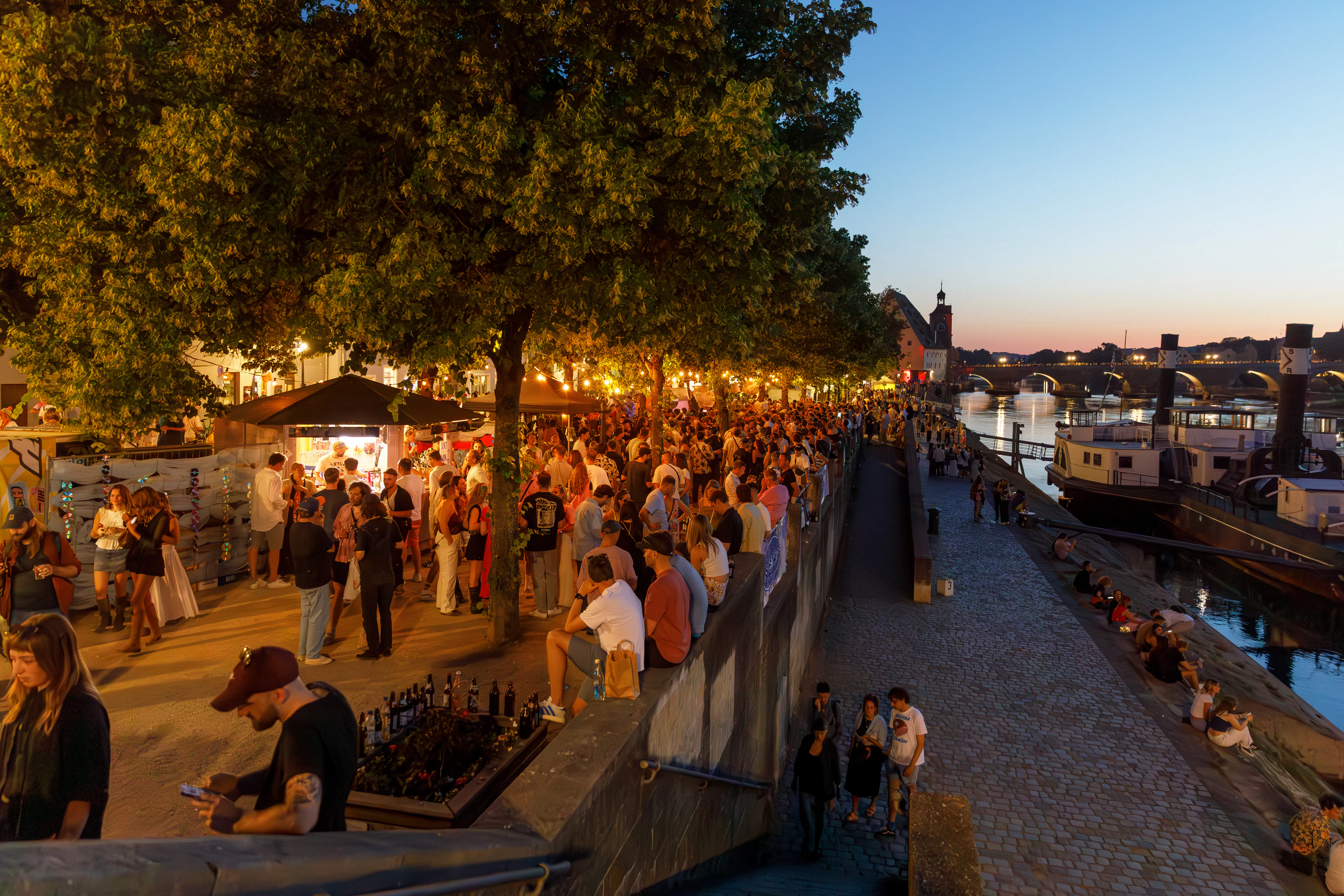 Menschenmenge am Donauufer, Steinerne Brücke im Hintergrund mit Sonnenuntergang