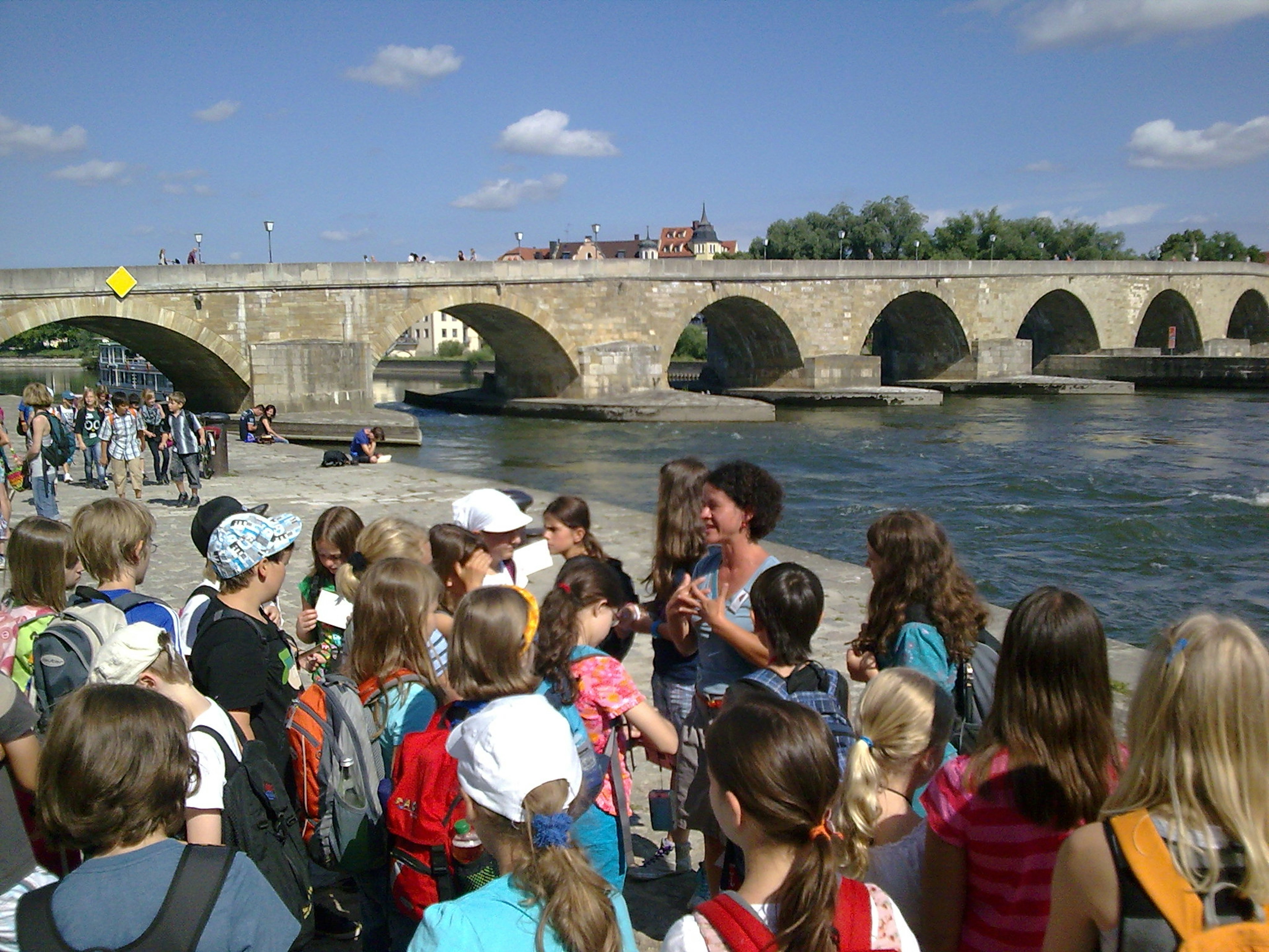 Schülergruppe steht vor dem Guide an der steinernen Brücke