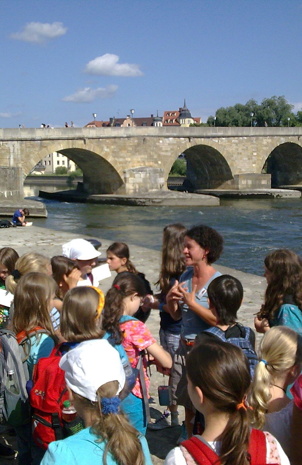 Schülergruppe steht vor dem Guide an der steinernen Brücke