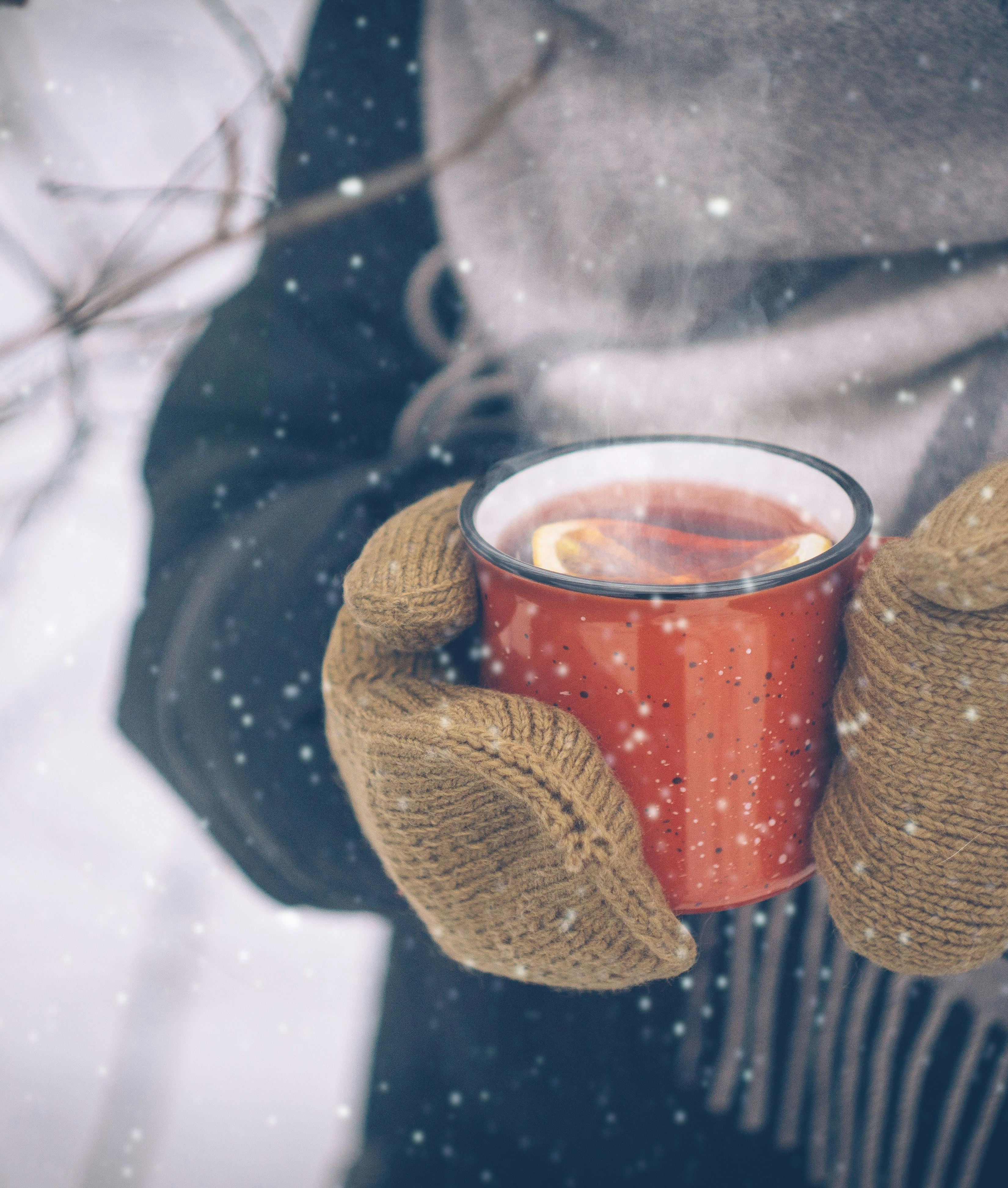 Hände in Handschuhen, die eine dampfende Tasse Punsch halten.
