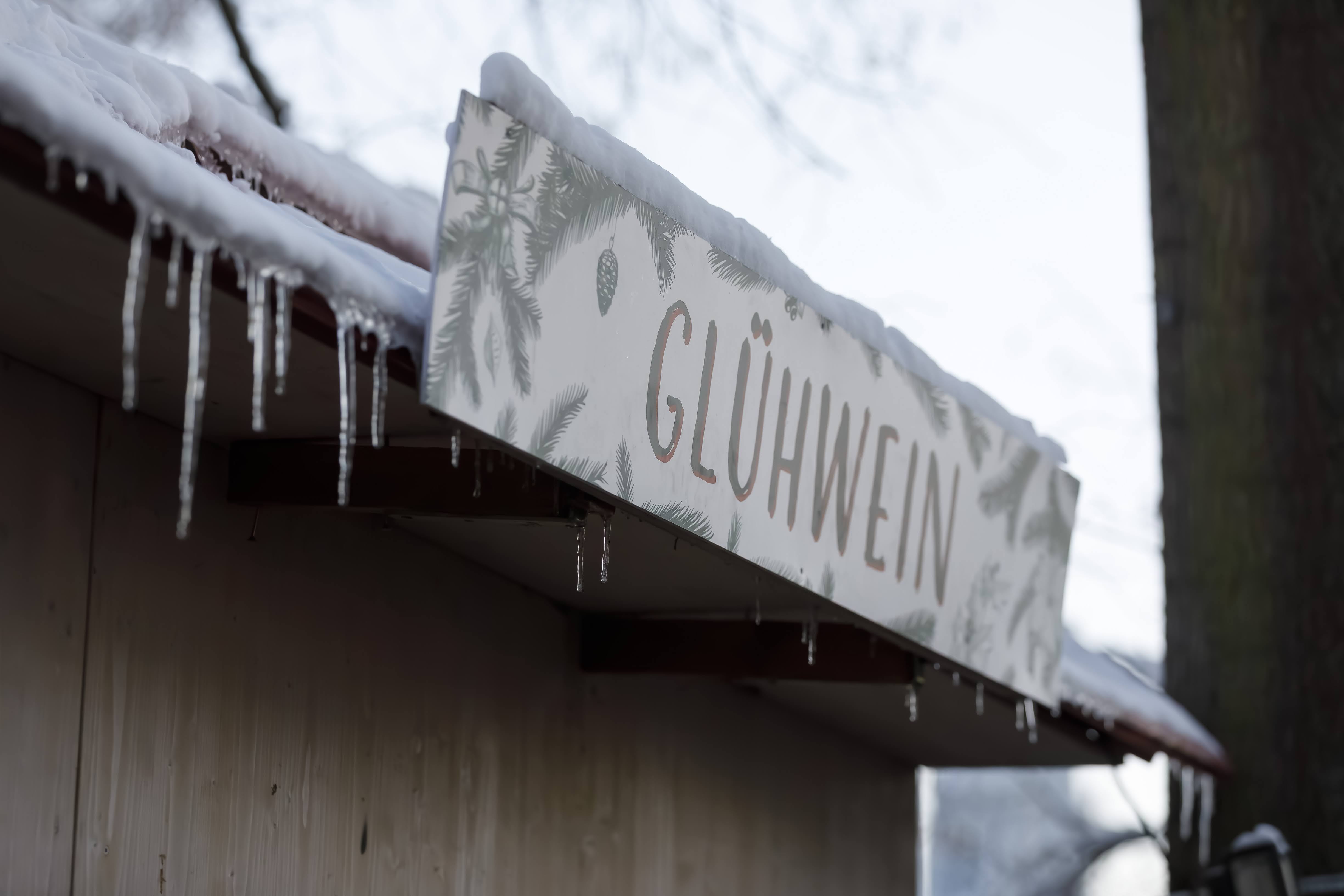 Glühweinschild am Dach einer Hütte mit Eiszapfen behangen