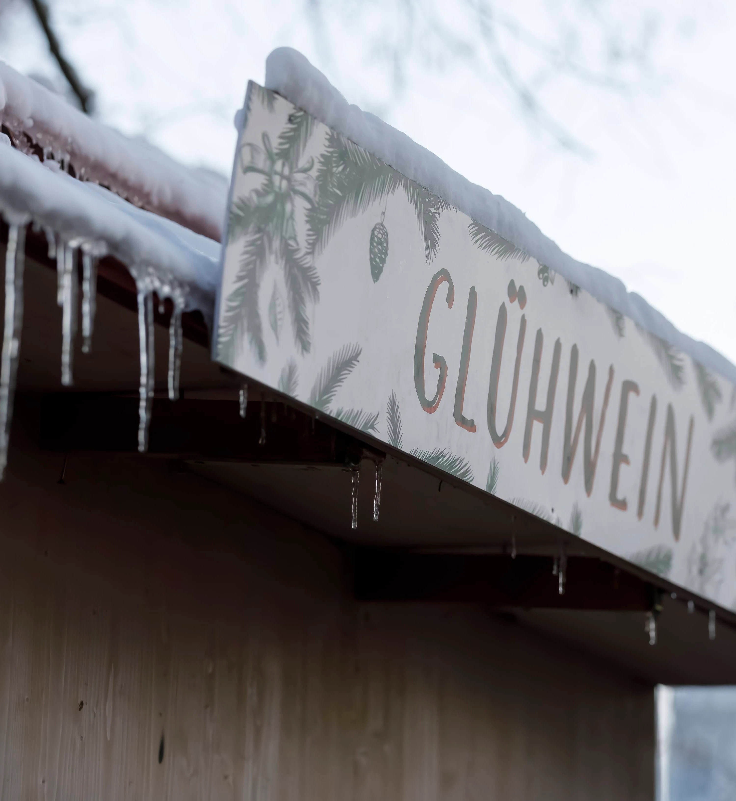 Glühweinschild am Dach einer Hütte mit Eiszapfen behangen