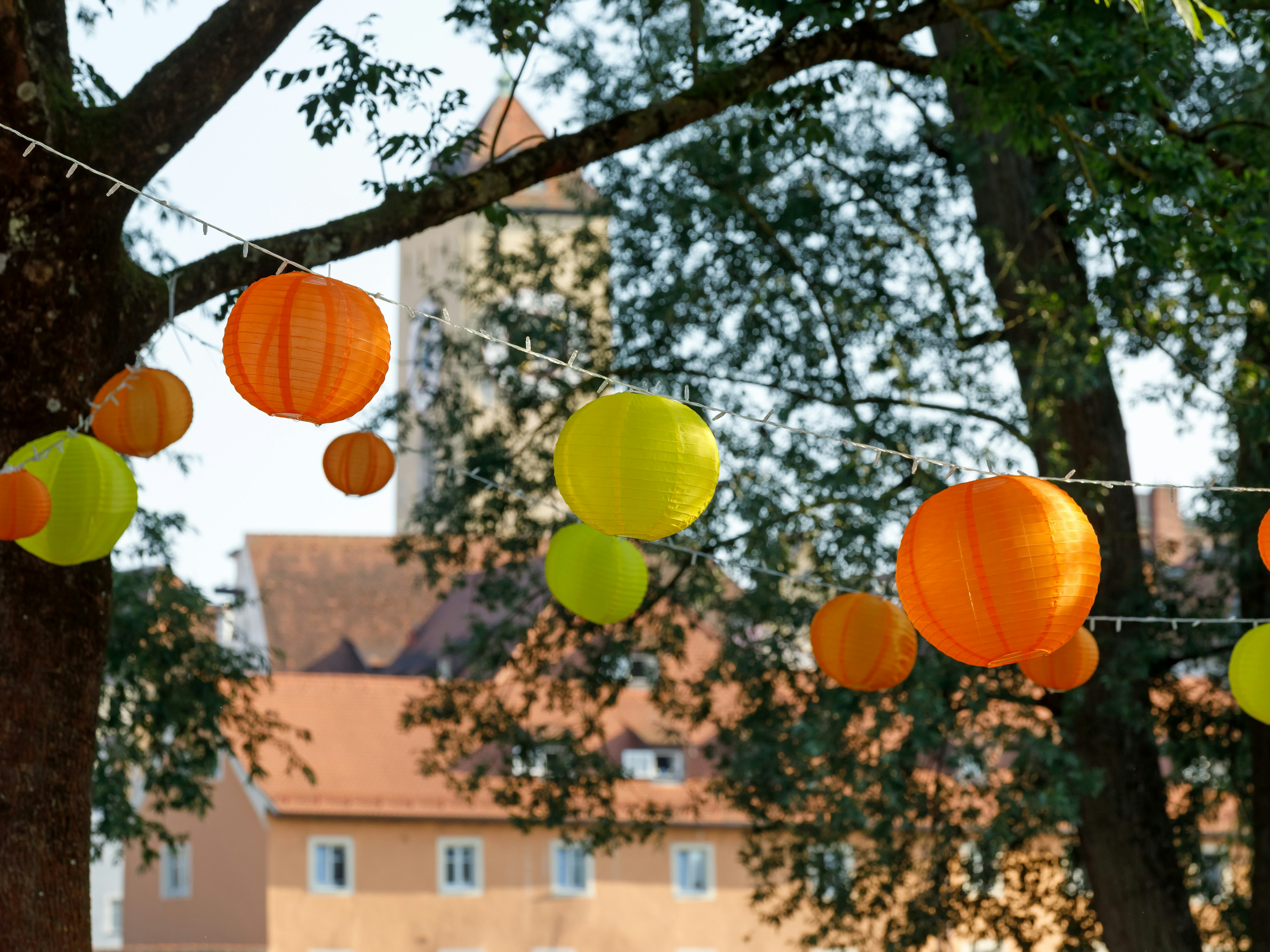 Lampions zwischen den Bäumen, im Hintergrund Häsuer und ein Turm