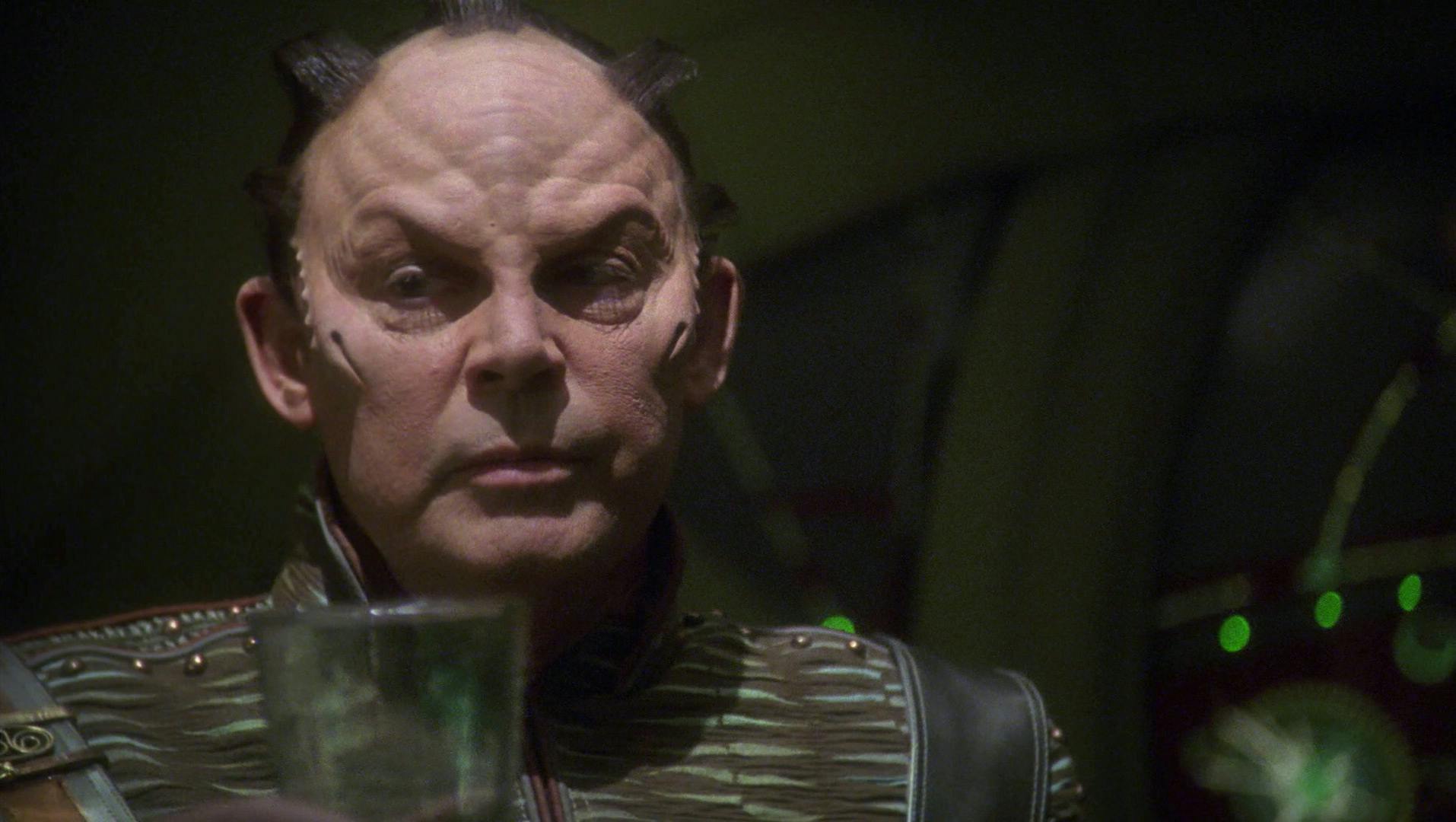 Close-up of Degra holding up a glass and looks over to his right in 'Azati Prime'